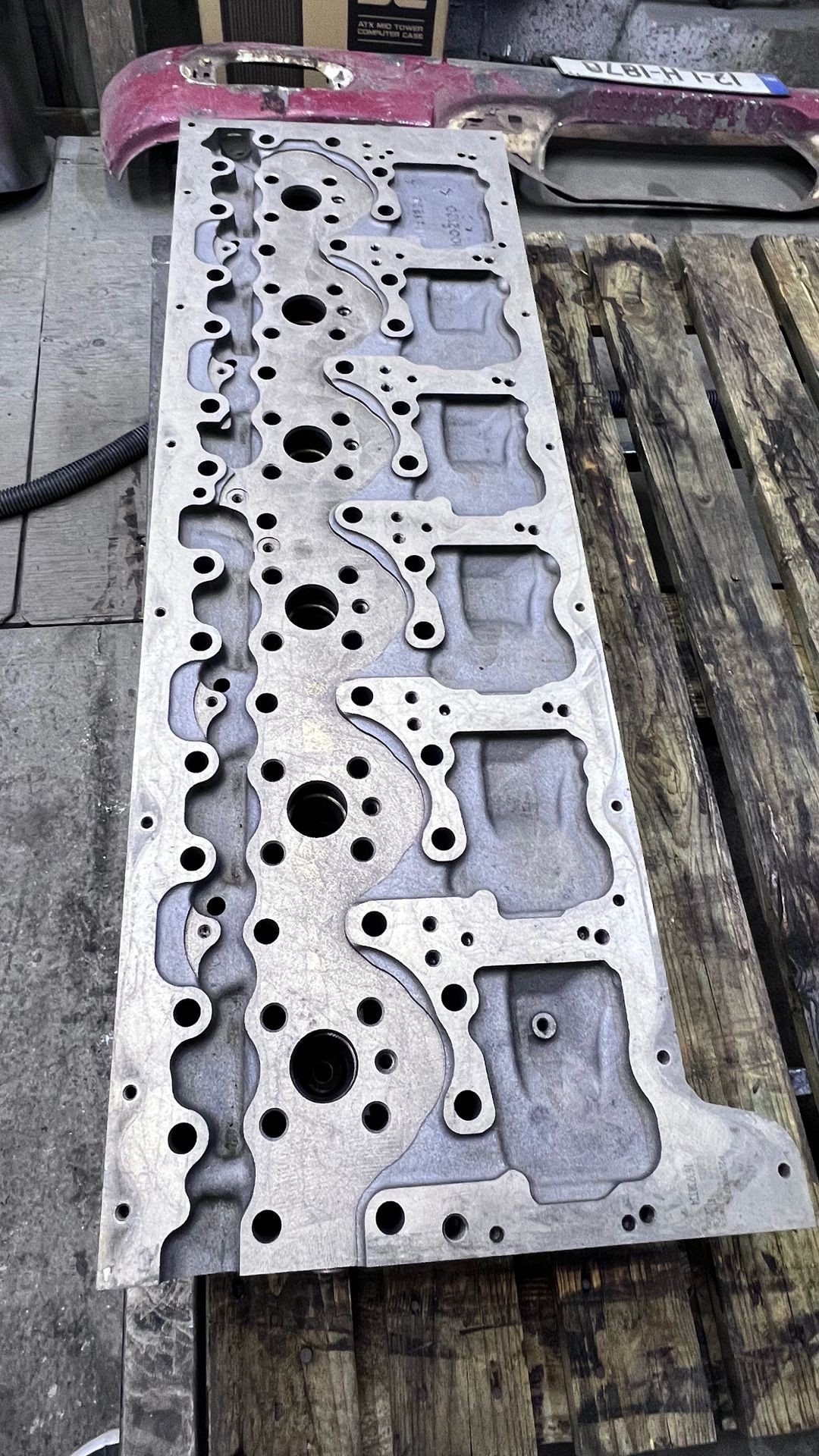 Metal engine head gasket placed on a wooden pallet within a workshop.