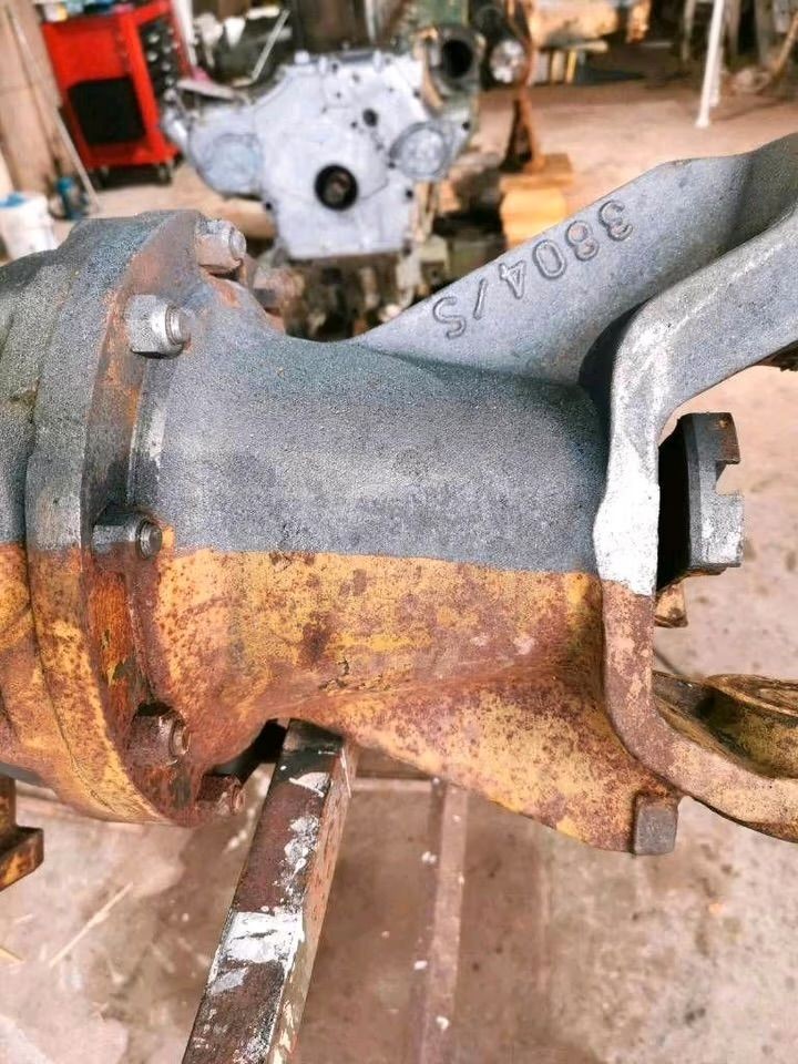 Close-up of a rusted metal automotive part with visible bolts, placed in a workshop environment.