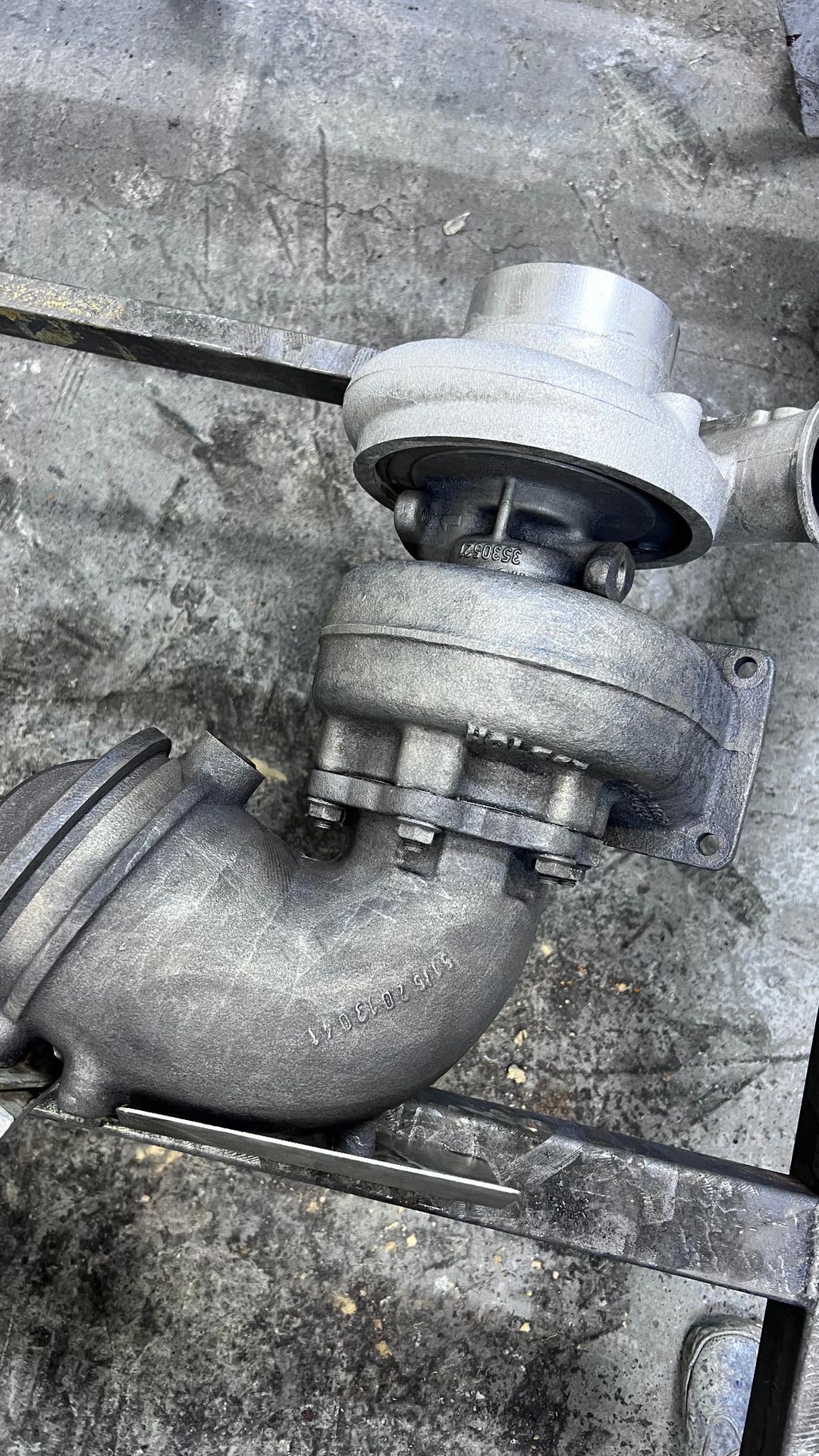 Close-up view of a metal turbocharger component lying on a concrete surface.